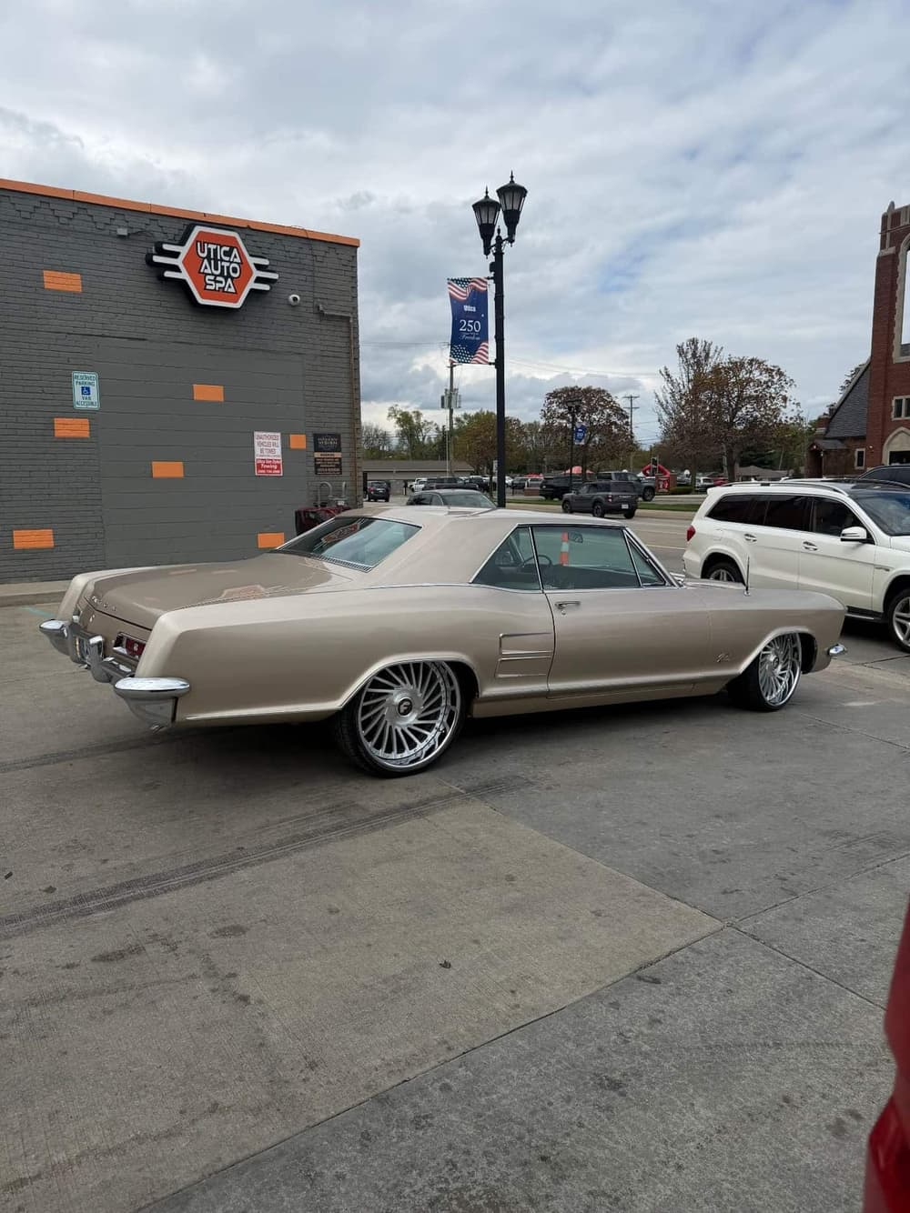 Rear three-quarter view of a 1963 Buick Riviera on Forgiato wheels parked at the Utica Auto Spa storefront on Van Dyke Ave