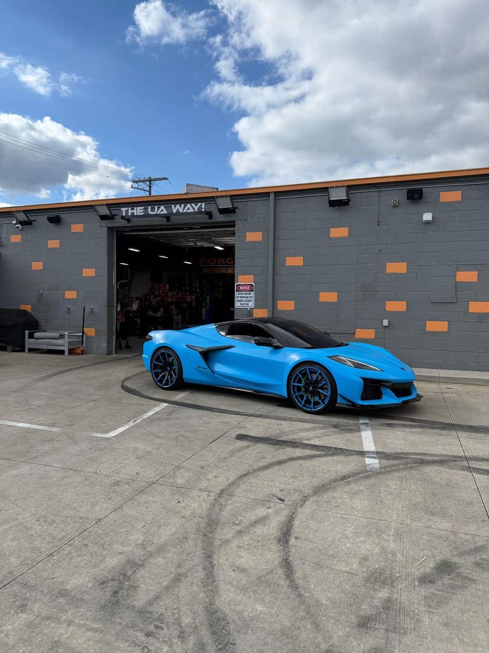 Side profile of a Riptide Blue wrapped Corvette Z06 on blue Forgiato wheels outside the Utica Auto Spa shop