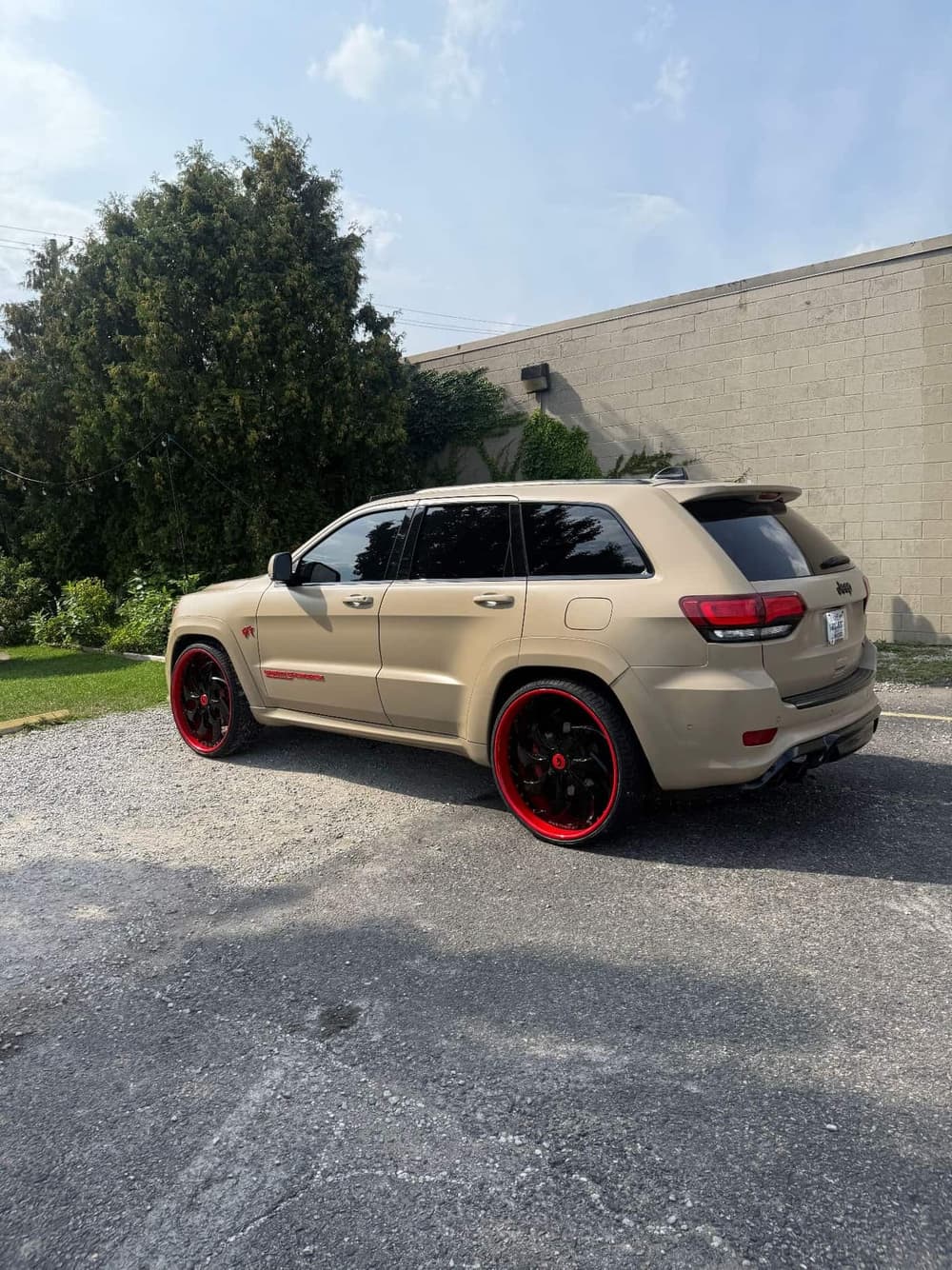 Rear three-quarter view of a matte tan wrapped Jeep Grand Cherokee SRT on red-lip black Forgiato wheels at Utica Auto Spa